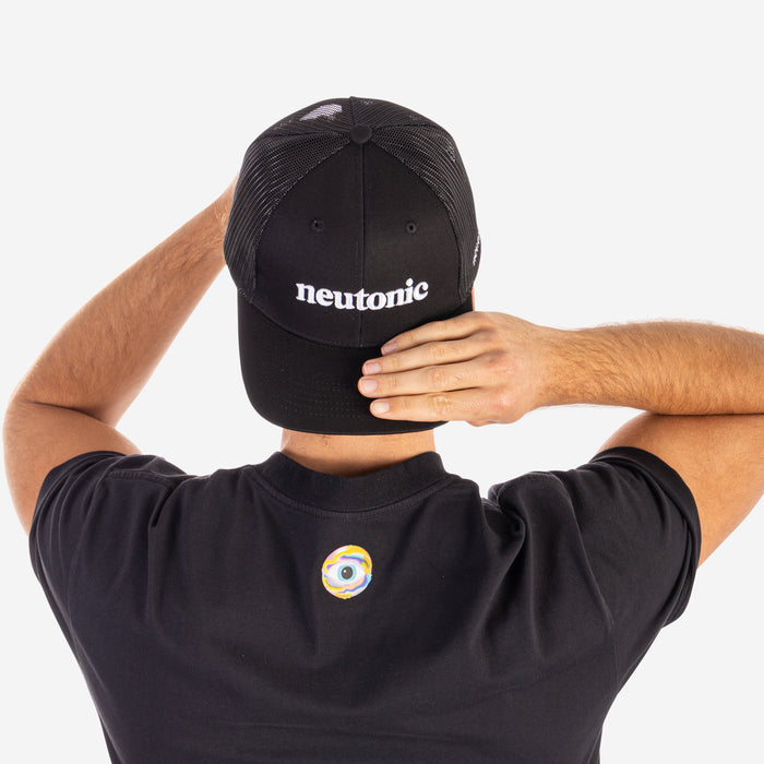 Black trucker cap with white "neotonic" logo, worn by person in black shirt with small colorful patch on back, emphasizing. - Neutonic - Trucker Cap